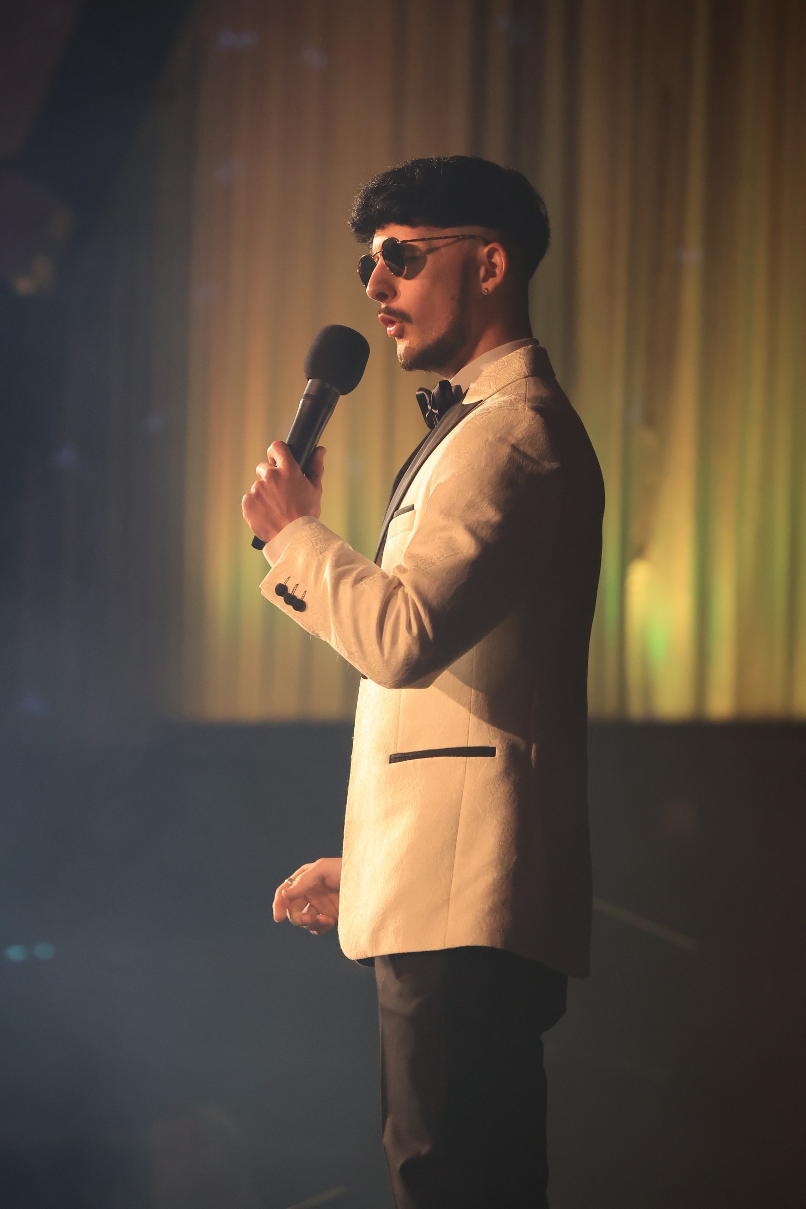 Jake Essex on stage, gold curtains