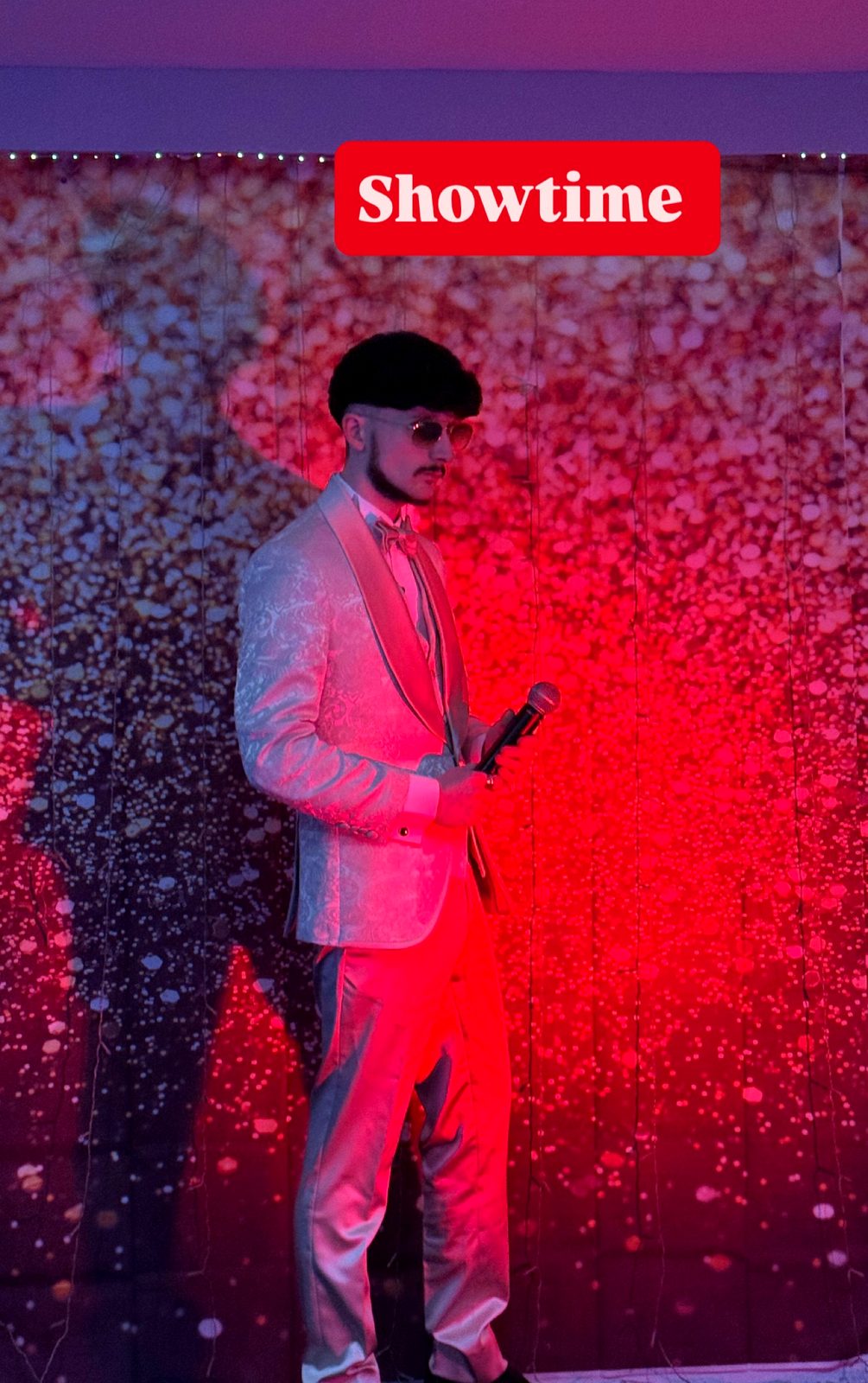 Jake Essex on stage in a champagne suit under red lights
