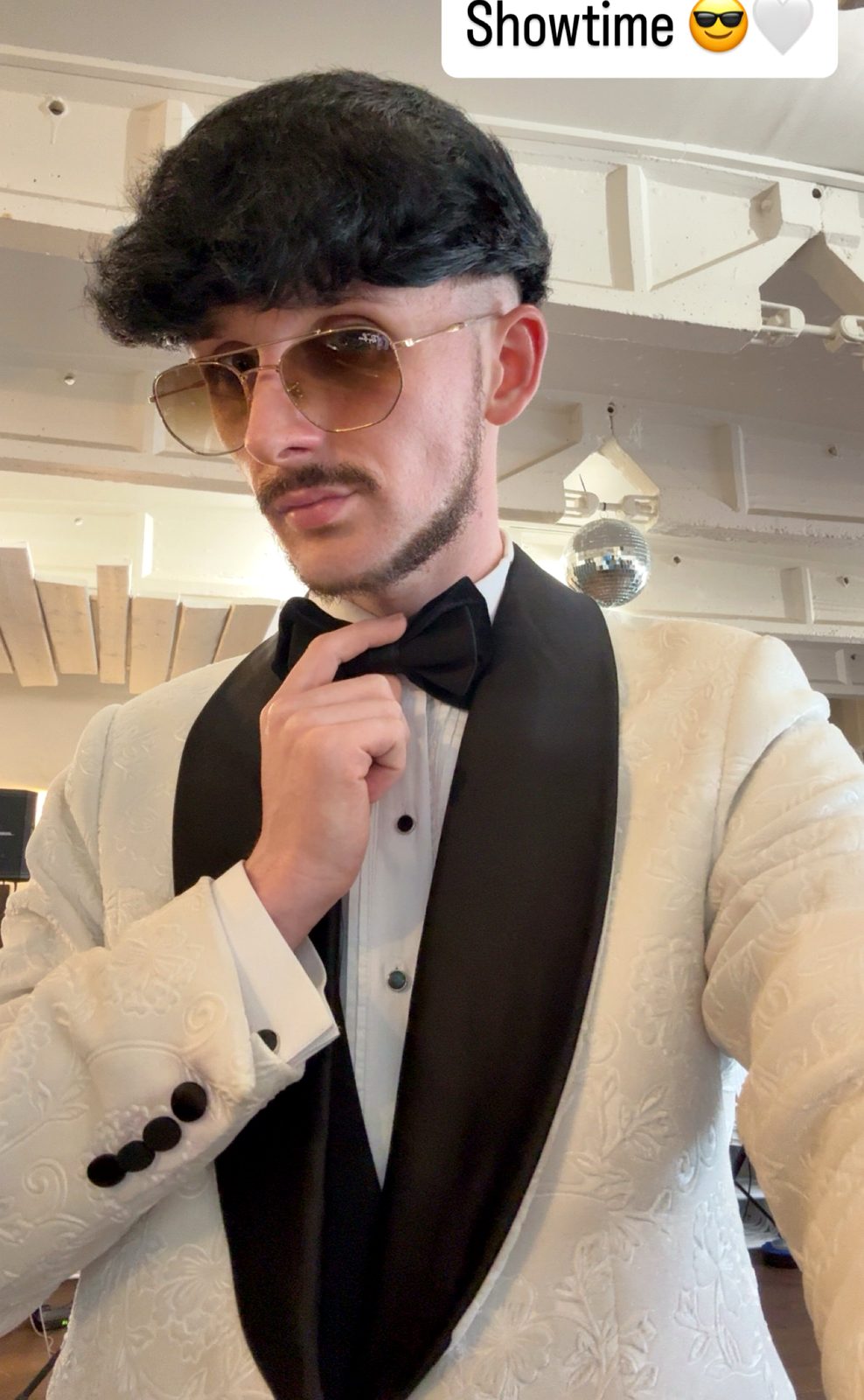 Jake Essex in a white dinner jacket and black bow tie under a disco ball